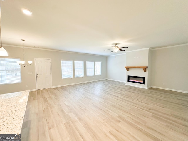 unfurnished living room with ornamental molding, ceiling fan with notable chandelier, a glass covered fireplace, light wood-style floors, and baseboards