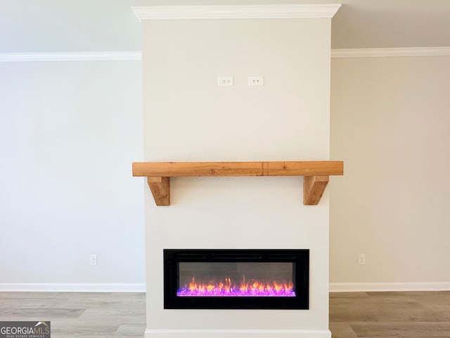 interior details featuring a glass covered fireplace, crown molding, baseboards, and wood finished floors