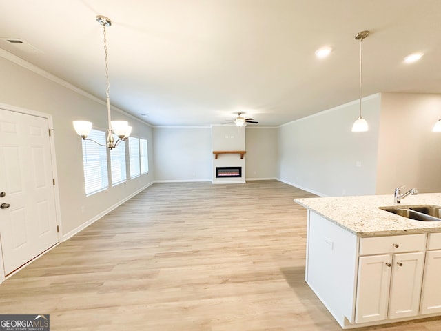 kitchen with pendant lighting, ornamental molding, ceiling fan with notable chandelier, light wood-style floors, and a sink