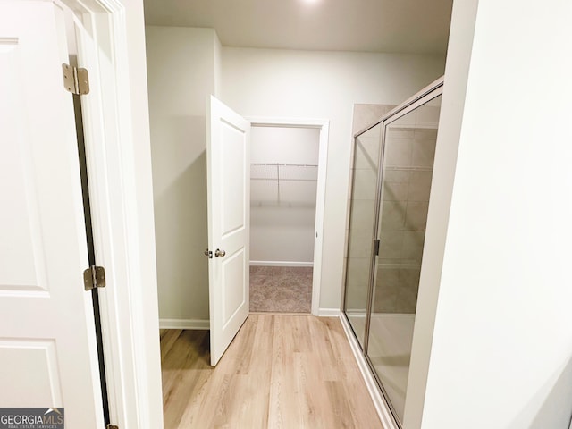 bathroom featuring a walk in closet, wood finished floors, baseboards, and a stall shower