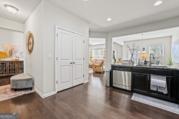 kitchen featuring dark wood-type flooring, a sink, baseboards, dishwasher, and light stone countertops