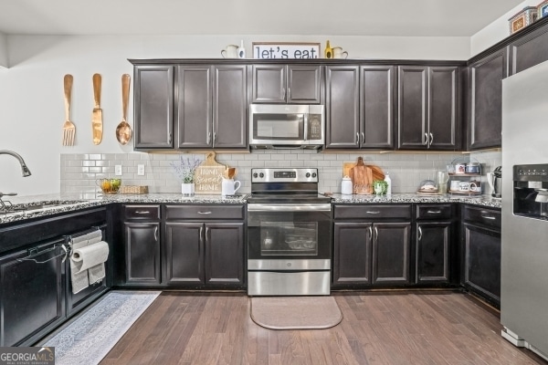 kitchen with dark wood-style floors, decorative backsplash, appliances with stainless steel finishes, and a sink