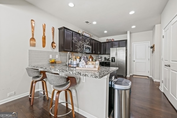 kitchen featuring a breakfast bar area, light stone counters, dark wood-style floors, a peninsula, and appliances with stainless steel finishes