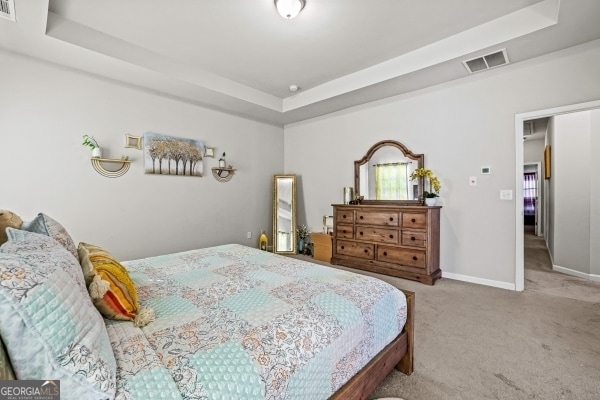 carpeted bedroom with a tray ceiling, baseboards, and visible vents