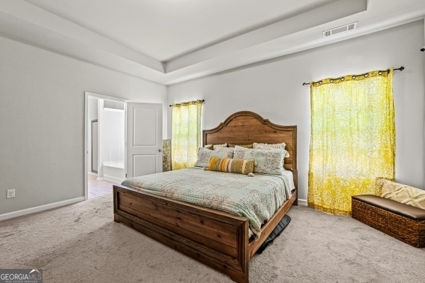 carpeted bedroom with a raised ceiling, baseboards, visible vents, and connected bathroom