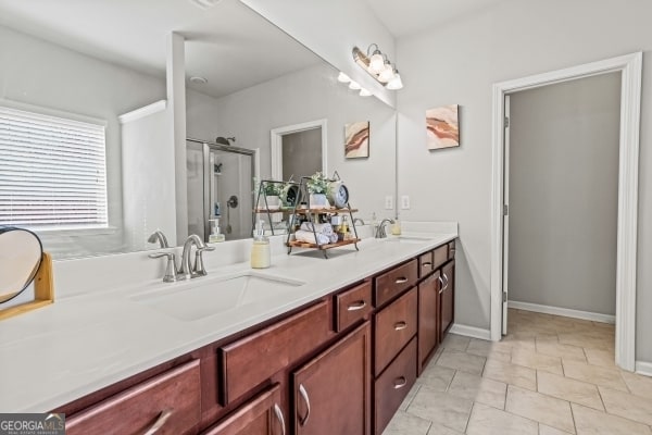 bathroom with a sink, double vanity, a shower stall, and tile patterned floors