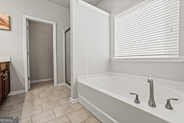 bathroom featuring tile patterned floors, baseboards, a stall shower, a bath, and vanity