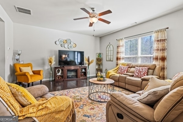 living area featuring visible vents, a fireplace, ceiling fan, and wood finished floors