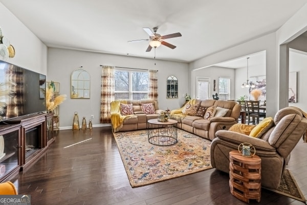 living area with a fireplace, ceiling fan with notable chandelier, dark wood-style floors, and baseboards