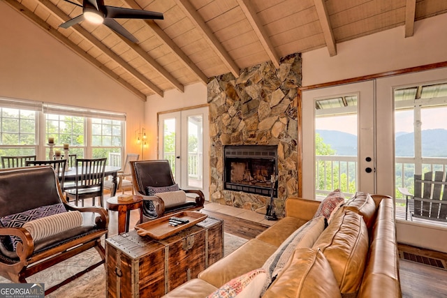 living area featuring a stone fireplace, french doors, visible vents, and wood finished floors