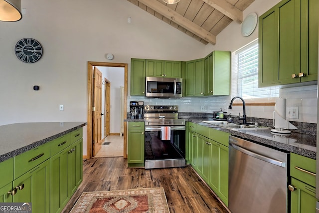 kitchen featuring green cabinetry, a sink, decorative backsplash, appliances with stainless steel finishes, and dark countertops