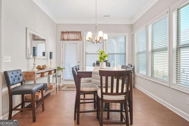 dining space featuring visible vents, crown molding, baseboards, an inviting chandelier, and wood finished floors