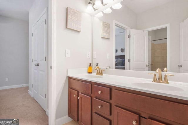 ensuite bathroom featuring double vanity, baseboards, and a sink