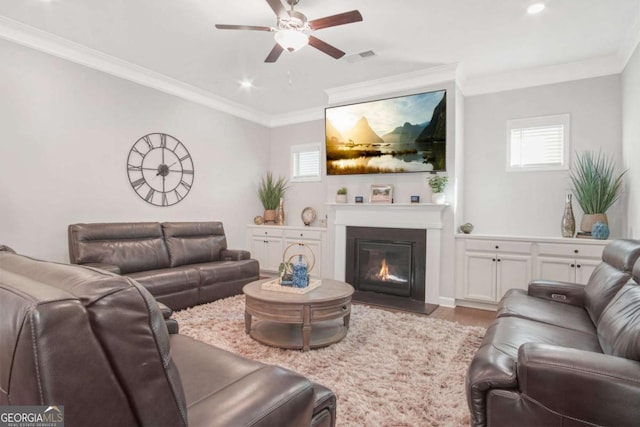 living area featuring visible vents, crown molding, ceiling fan, wood finished floors, and a glass covered fireplace