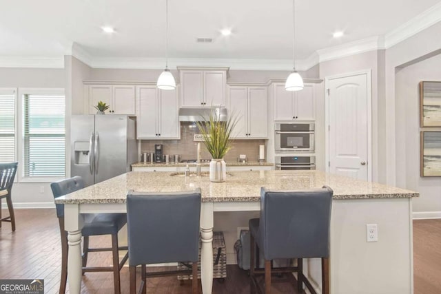 kitchen featuring a large island, ornamental molding, under cabinet range hood, appliances with stainless steel finishes, and a breakfast bar area