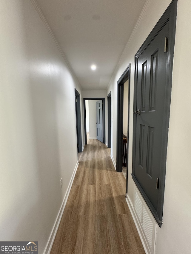 corridor featuring wood finished floors, baseboards, and ornamental molding