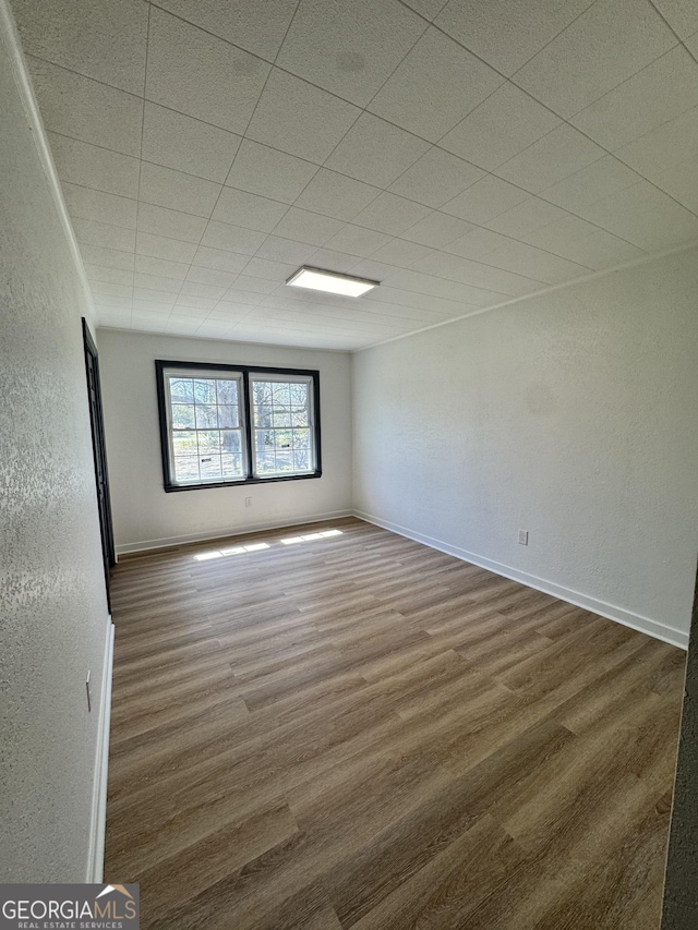 spare room featuring baseboards, wood finished floors, and a textured wall