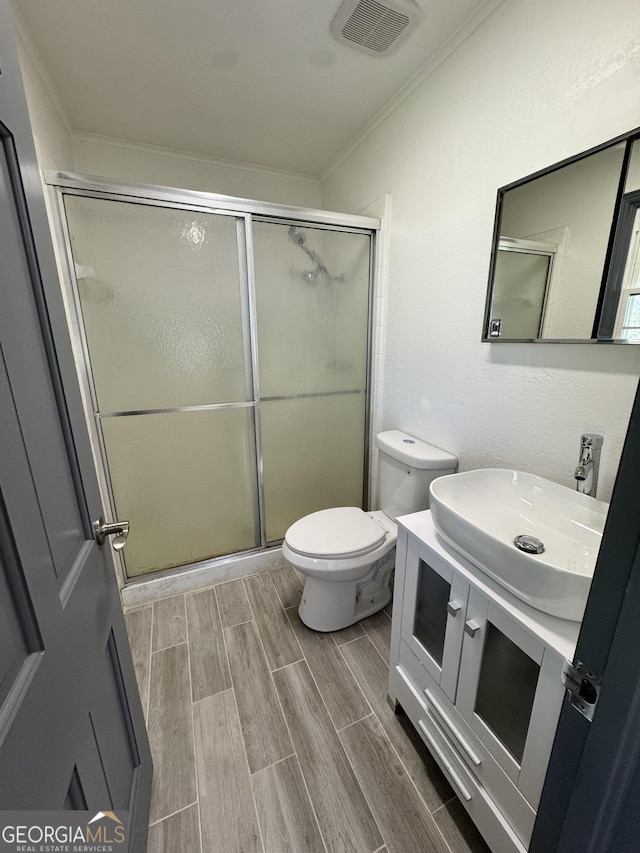 full bathroom featuring wood finish floors, visible vents, toilet, a stall shower, and ornamental molding