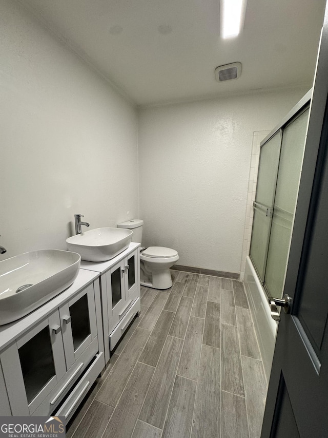 bathroom with visible vents, wood tiled floor, toilet, double vanity, and a sink