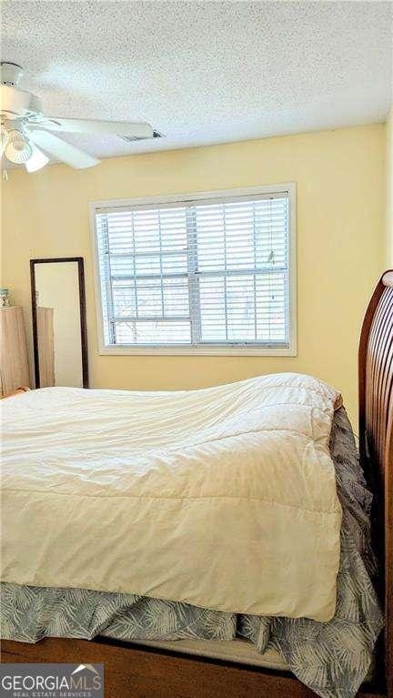 bedroom featuring visible vents, a textured ceiling, and a ceiling fan