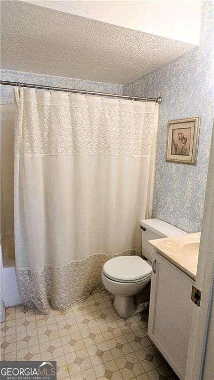 bathroom with toilet, curtained shower, a textured ceiling, and vanity