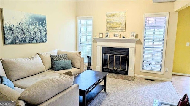 living room with baseboards, plenty of natural light, visible vents, and a fireplace with flush hearth