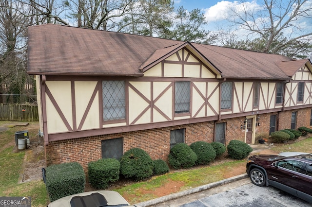 tudor home featuring brick siding, stucco siding, cooling unit, and roof with shingles