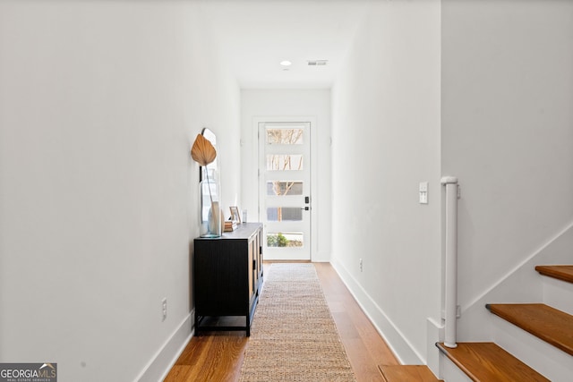 corridor featuring light wood-type flooring, baseboards, visible vents, and stairs