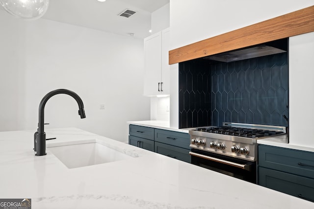 kitchen with visible vents, a sink, decorative backsplash, stainless steel stove, and white cabinetry