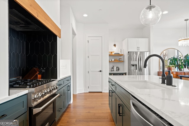 kitchen with light wood-style flooring, a sink, light stone counters, stainless steel appliances, and wall chimney exhaust hood