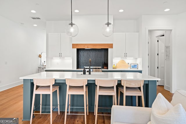 kitchen with visible vents, light wood-style flooring, a center island with sink, a sink, and light countertops