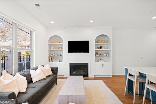 living room featuring visible vents, built in features, recessed lighting, a fireplace, and light wood-style floors