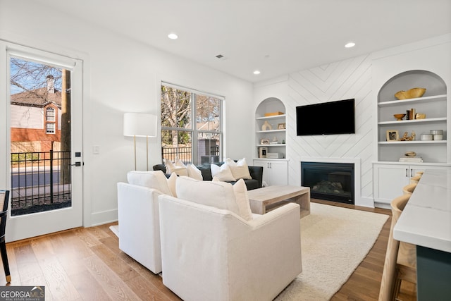 living room featuring baseboards, built in features, recessed lighting, a fireplace, and wood finished floors