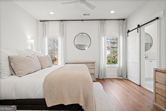 bedroom featuring wood finished floors, visible vents, ensuite bath, recessed lighting, and a barn door