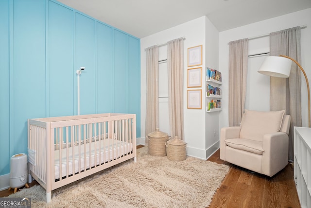 bedroom with baseboards, a nursery area, and wood finished floors