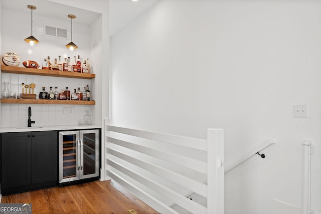 bar featuring visible vents, beverage cooler, indoor wet bar, wood finished floors, and a sink