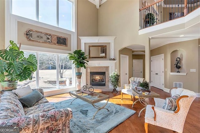 living room with visible vents, wood finished floors, a glass covered fireplace, and a towering ceiling