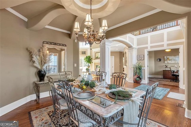 dining area with a notable chandelier, ornamental molding, wood finished floors, a towering ceiling, and ornate columns