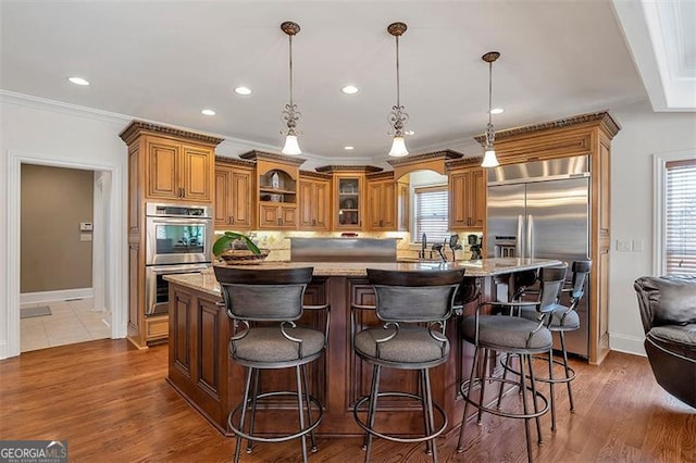 kitchen with backsplash, crown molding, light stone countertops, appliances with stainless steel finishes, and brown cabinetry