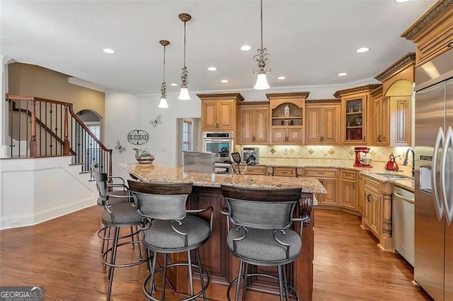 kitchen featuring backsplash, wood finished floors, brown cabinetry, stainless steel appliances, and a sink