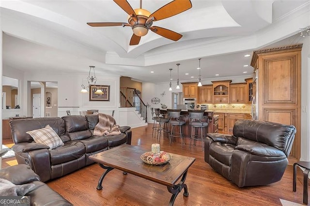 living area with crown molding, stairs, a tray ceiling, wood finished floors, and a ceiling fan