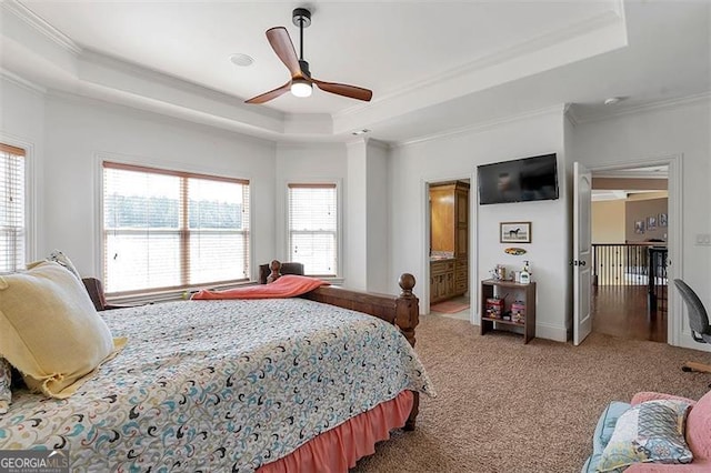 carpeted bedroom featuring a tray ceiling, connected bathroom, crown molding, and ceiling fan