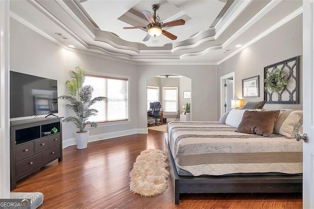 bedroom featuring a raised ceiling, wood finished floors, arched walkways, crown molding, and baseboards