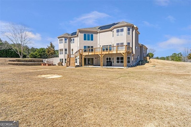 back of property with stucco siding, roof mounted solar panels, and a deck