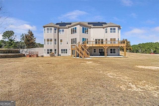 rear view of house featuring a wooden deck, stucco siding, stairs, a patio area, and roof mounted solar panels