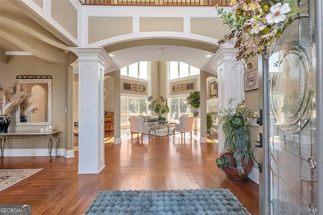 entrance foyer featuring arched walkways, a high ceiling, ornate columns, and wood finished floors