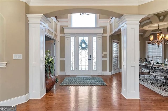 entryway with decorative columns, wood finished floors, a chandelier, and ornamental molding