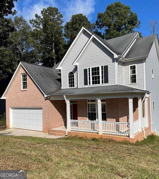 view of front of property with driveway, a front lawn, a porch, an attached garage, and brick siding