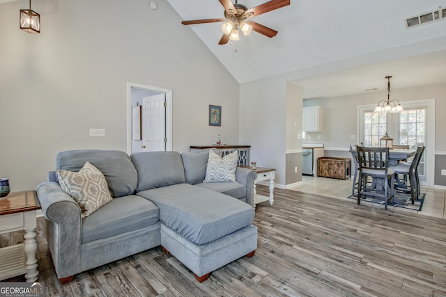 living room featuring visible vents, high vaulted ceiling, ceiling fan with notable chandelier, light wood finished floors, and baseboards