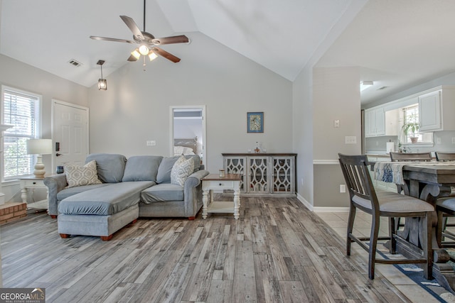 living area with visible vents, high vaulted ceiling, light wood finished floors, baseboards, and ceiling fan